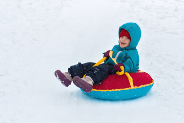 Fototapeta na wymiar happy child. little boy in winter ride on a sled from the mountain. Kid long and happy smiles and have fun.
