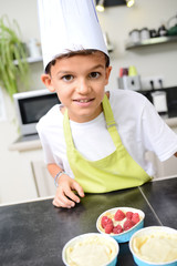 beautiful young happy boy child kid cooking a fun cake in kitchen at home