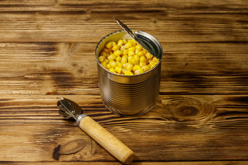 Open tin can of corn and can opener on wooden table