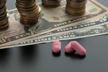 Three pink pills, tablets with dollar bills and stacks of coins on the background. Concept of...