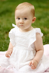 Cute baby girl with beautiful eyes sitting outside on a blanket 