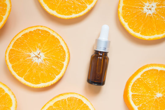 Natural vitamin c serum, skincare, essential oil products. Cosmetic brown glass vial w/ dropper and fresh juicy orange fruit slice on orange background. Beauty product branding mock-up. Top view.