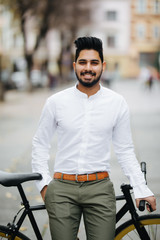 Portrait of young indian man with brown hair walking with fix bicycle on street