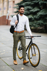 Portrait of cheerful young asian guy walking outdoors with bicycle holding backpack.