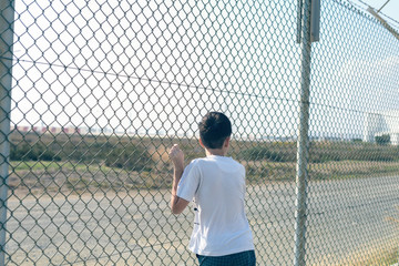 A barefoot boy stands on the beach near the iron net and looks at the airport.