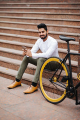 Smiling asian businessman on break, sitting on stairs smartphone, resting after bicycle ride, copy space