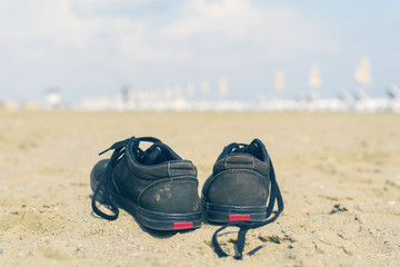 Black sneakers on the sandy beach on the sea background. Summer and travel concept