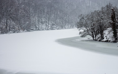 Fototapeta premium Frozen winter lake with cold forest in Lillafured, Miskolc, Hungary. Lake with ice and snowy mountain. Winter landscape. Travel in Hungary. Winter weather concept. Snowy mountain in frosty fog.