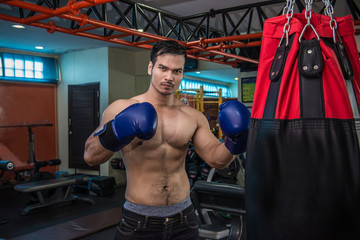 Handsome muscular man in boxing gloves punching bags in gym