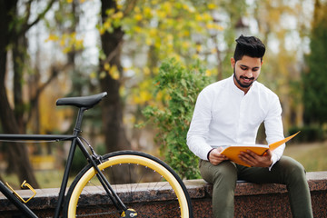 Young indian man reading a book while taking a break on the city street