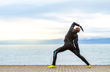 Girl runner in black sportswear stretching by the lake in the winter morning