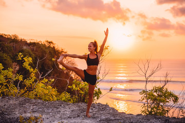 Young sporty girl practicing yoga at warm sunset time