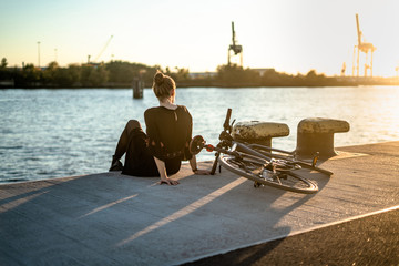 Young woman with her bicycle in harbour while sunset