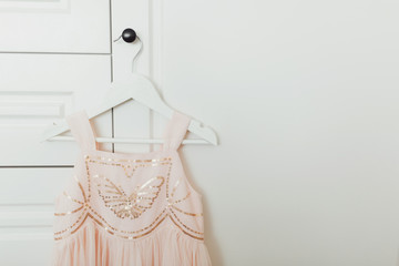 Beautiful dressy lush pink dress for girls on hanger at the background of white wardrobe. Kids dresses with sequins for prom and holiday.