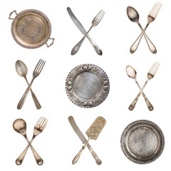 A set of crossed vintage spoons, forks, knives and silver old plates. Isolated on white