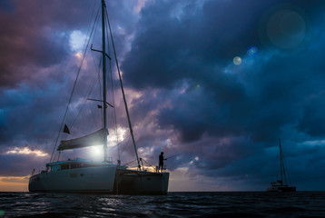 The dark silhouette of catamarans on open sea with dramatic clouds during sunset. The fisherman...