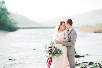 Beautifull wedding couple kissing and embracing near the shore of a mountain river with stones