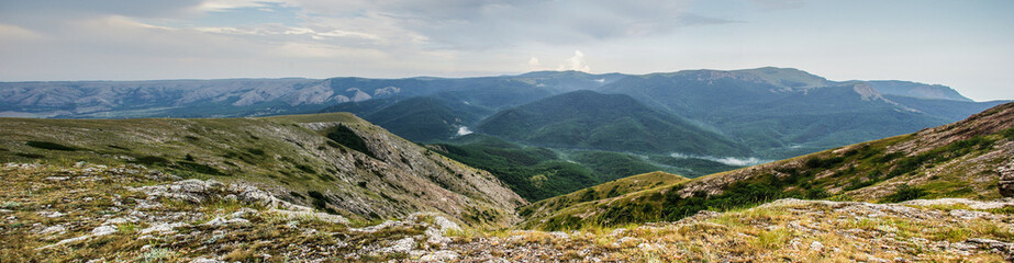 Panorama of the Crimean Highlands. View from the plateau to wooded slopes and distant mountains. Mist rises from the forest