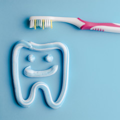 Toothpaste in a form of a smiling tooth with a pink toothbrushe on blue. Toothpaste on blue. Dental hygiene.
