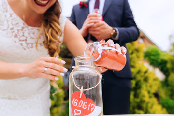 close-up of unity vase on which heart with the date of the wedding and the bride is pouring red sand into the jar