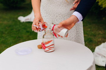 the newlyweds together pour white and red sand into a unity vase.