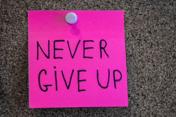 Never give up write in pink sticker notes over cork board background.