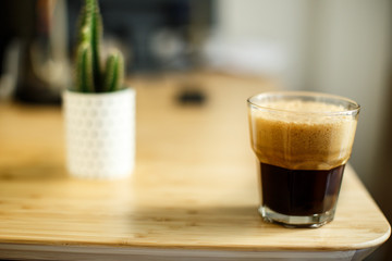 A glass of iced espresso lying on a wooden table in front of a desk cactus