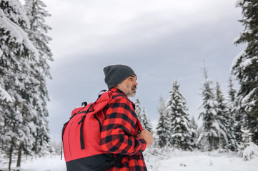 Fototapeta na wymiar Traveler with a backpack in a warm jacket looks at the winter forest