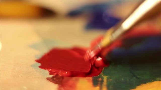 Artist lowers the brush in red paint and mixes it on the palette.Macro shooting.
