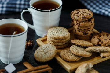 Two cups of tea and various cookies on dark wooden background