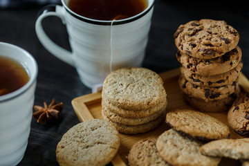 Two cups of tea and various cookies on dark wooden background