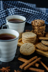 Two cups of tea and various cookies on dark wooden background