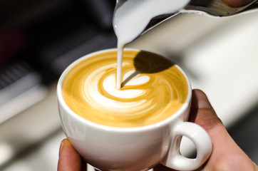 Holding espresso cup and pouring milk to make latte art shapes