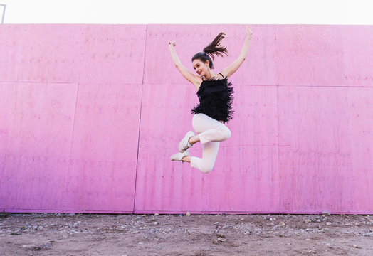 Exuberant young woman jumping in front of pink wall