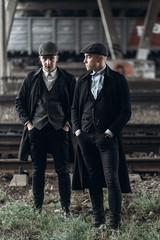 stylish gangsters men, posing on background of railway. england in 1920s theme. fashionable brutal...