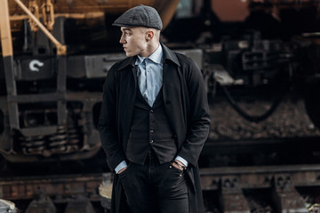 Fototapeta na wymiar stylish gangster man posing on background of railway. england in 1920s theme. fashionable brutal confident guy. atmospheric moments. space for text
