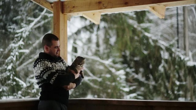 A young guy on the porch in the winter plays with cat