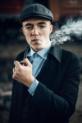 stylish gangster smoking in tweed look, posing on background of railway. england in 1920s theme....