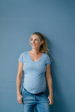Portrait of smiling pregnant woman standing at blue wall