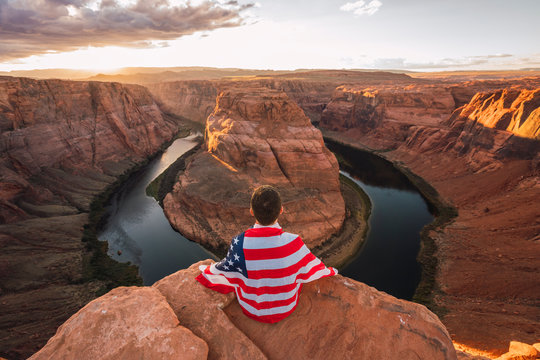 USA, Arizona, Colorado River, Horseshoe Bend, young man sitting on viewpoint with American flag