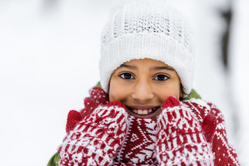 close up view of african american child in knitted hat, mittens and scarf smiling and looking at camera in winter