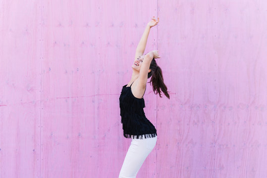 Happy young woman standing in front of pink wall