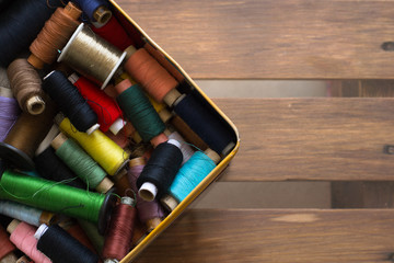 Fototapeta na wymiar Box with many colorful sewing threads on wooden table. Top view.
