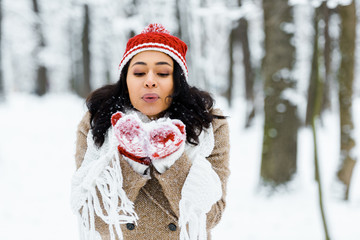 beautiful african american woman blowing snow in winter forest