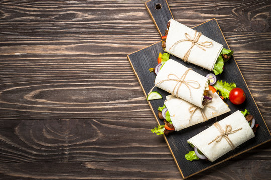 Burritos tortilla wraps with beef and vegetables on wooden backg