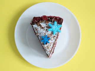 Chocolate cake slice with snowflakes decoration and cherry on winter background top view.