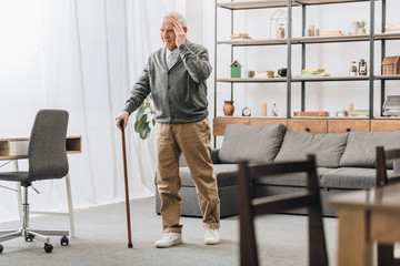 senior man standing with walking cane while having headache