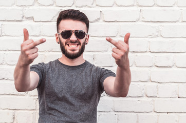 Portrait of a handsome young man standing against a white brick wall. Smile, indecent gestures.