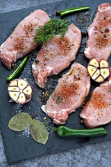 Fresh, raw, seasoned pork steaks on a stone board