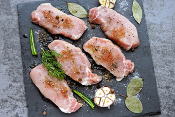 Fresh, raw, seasoned pork steaks on a stone board